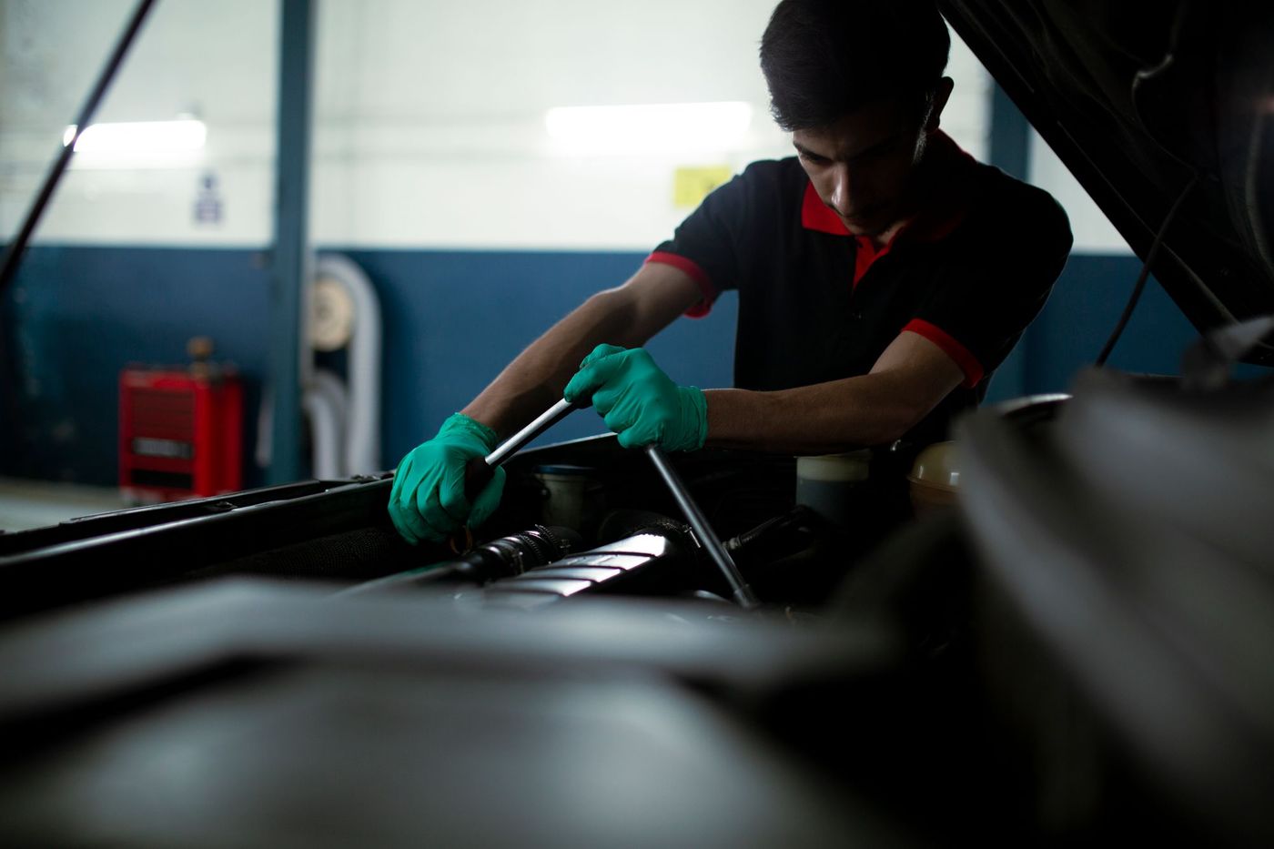 Mechanik v zelených rukavicích pracuje pod otevřenou kapotou auta