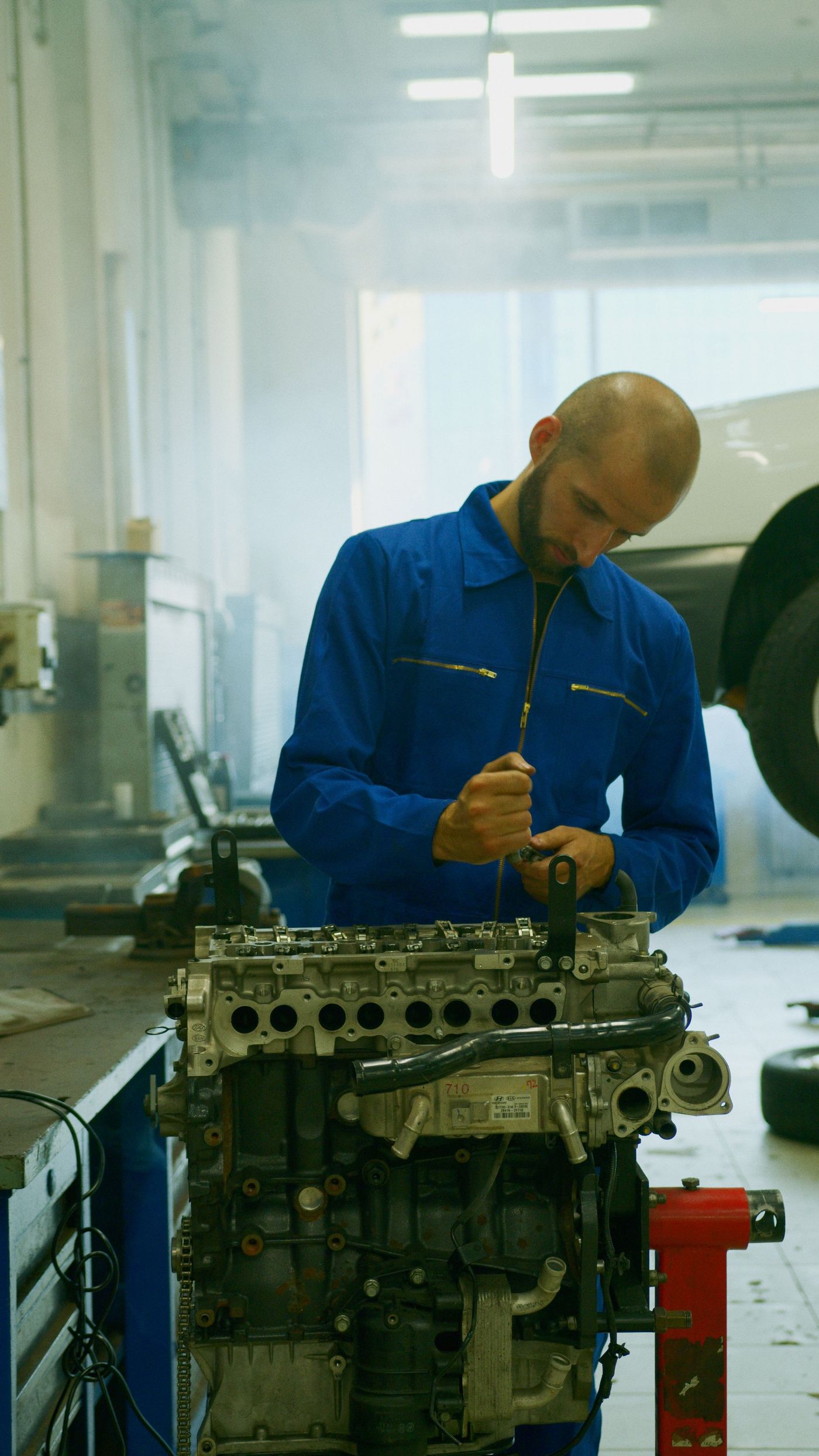 Mechanik v modré kombinéze pracuje na rozebraném motoru