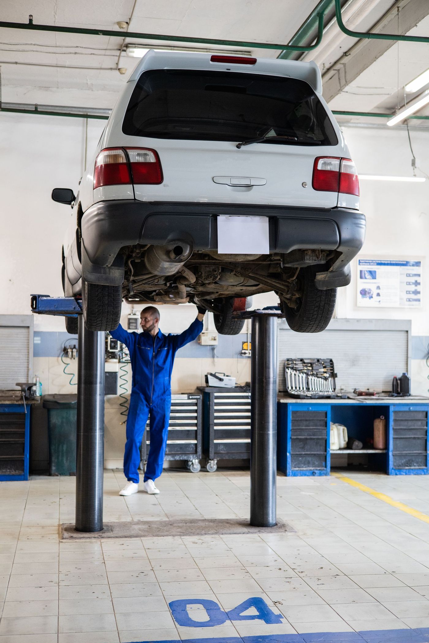 Auto na zvedáku v servisu a mechanik v modré kombinéze pod ním