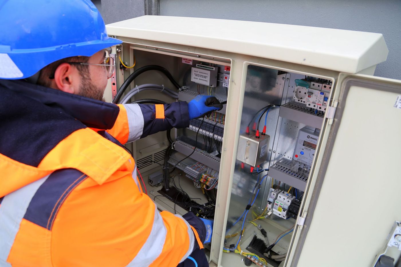 Elektrikář v přilbě a reflexní bundě pracuje u elektroměrového rozvaděče